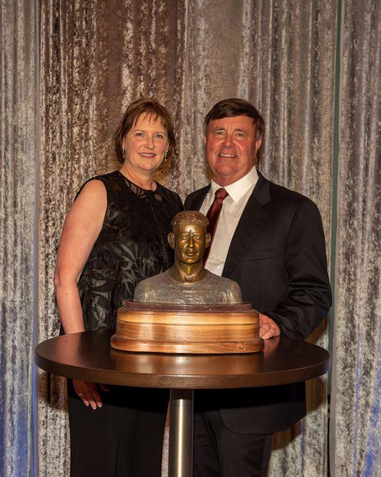 Robyn and Alan roberts standing in front of a bust of E. King Gill