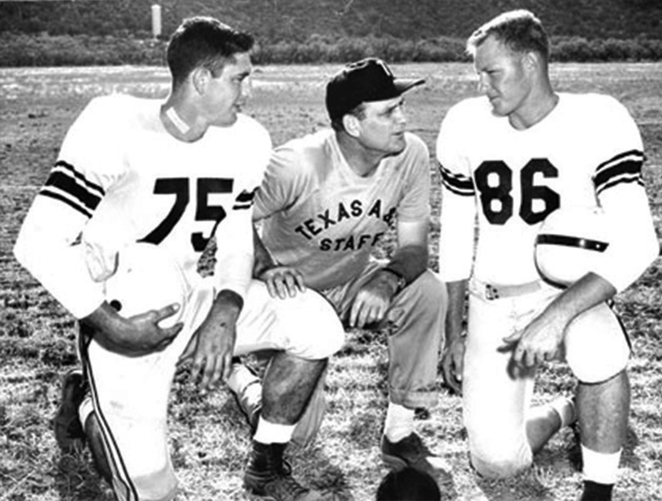 Two football players kneeling and looking at their coach