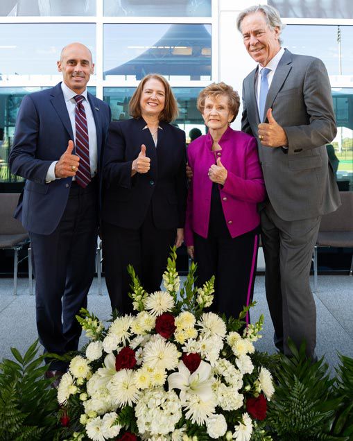 Two men and two women standing in front of flowers giving thumbs up